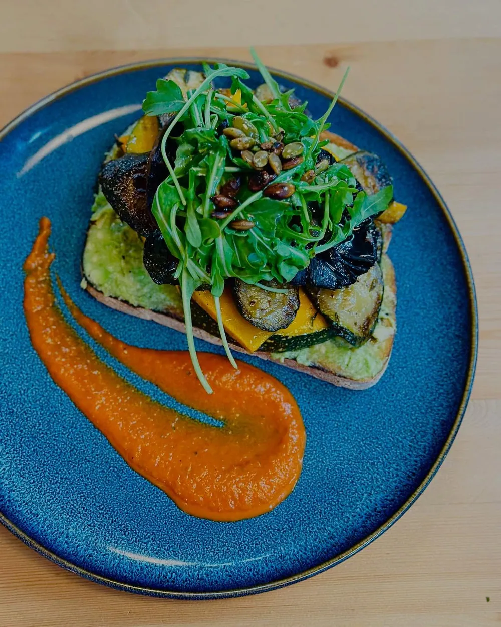 Avocado and greens on toast with a romesco swoosh, on a deep blue plate