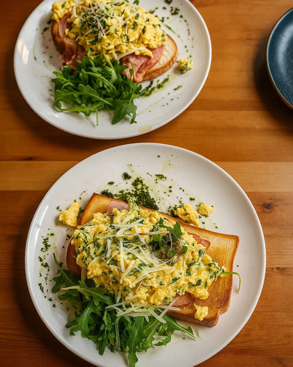Two plates of scrambled eggs on toast with rocket and shaved parmesan